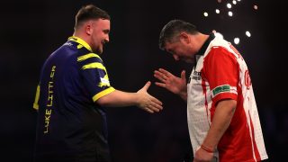 Luke Littler (balra) és Mensur Suljovic kezet ráznak, miután előbbi nyert a dartsvilágbajnokságon, Londonban.