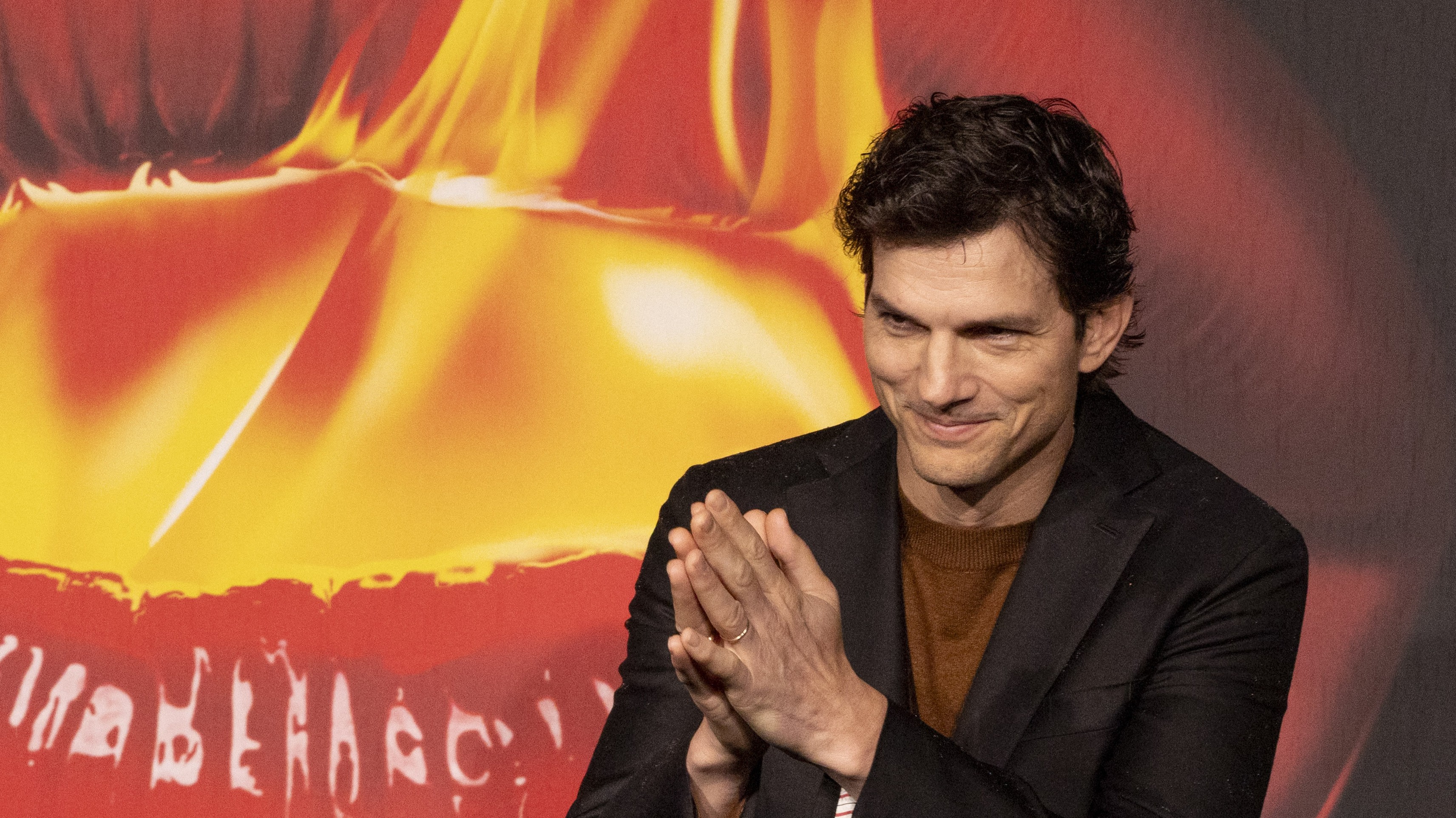 Ashton Kutcher a kezeit összetéve mosolyog egy premiervetítés vörös szőnyegén