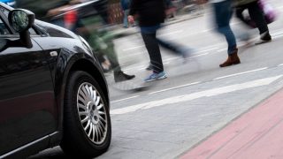 A kép egy autót ábrázol, mely egy zebra előtt fékez, ahol gyalogosok haladnak át éppen.