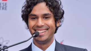 Kunal Nayyar egy mikrofon mögött állva mosolyog, egy világos háttér előtt