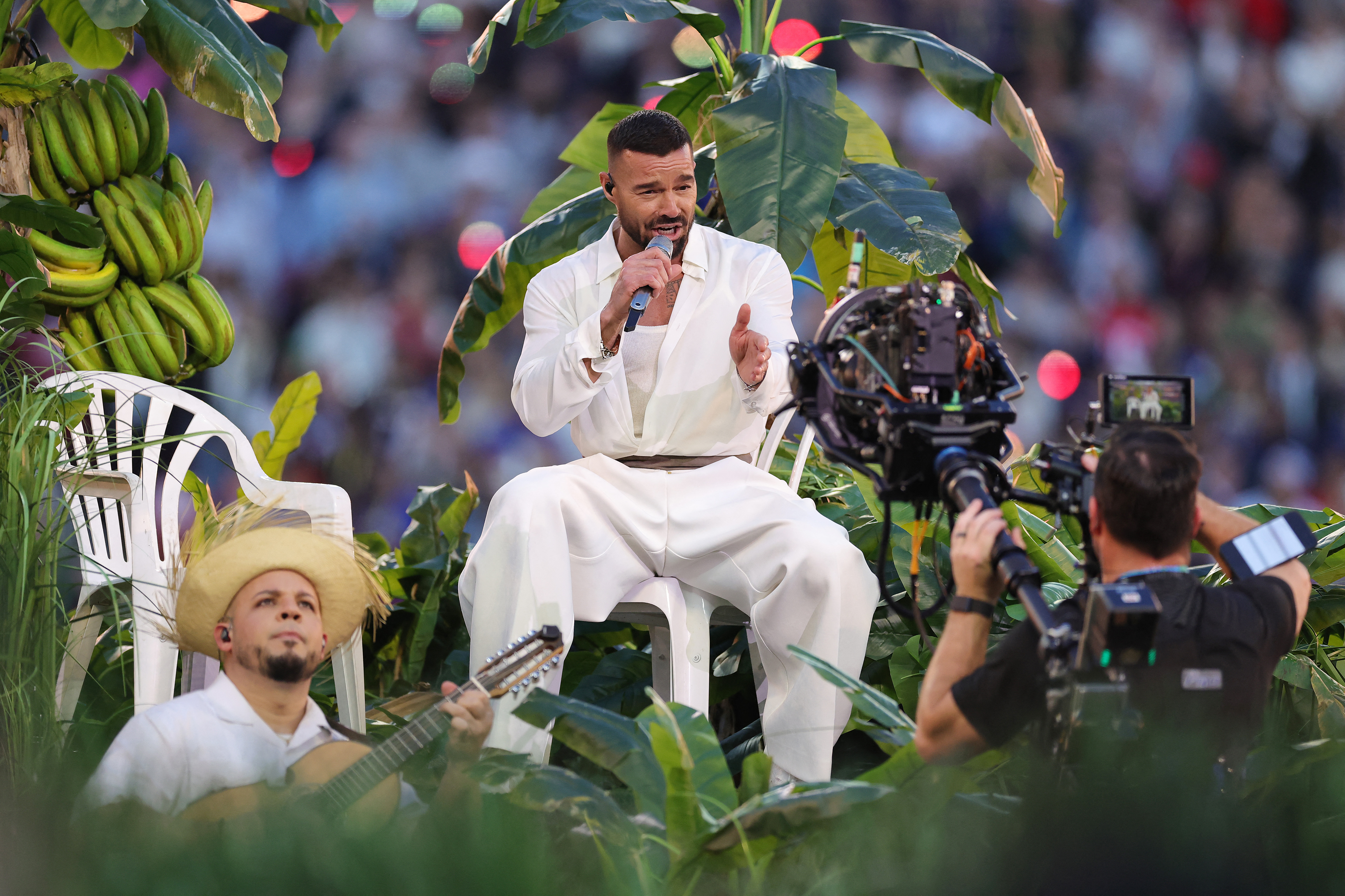 Ricky Martin egy székben ülve, növényekkel körbevéve énekel a színpadon