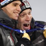 Gold medallists Austria's Stephan Embacher (L) and Austria's Jan Hoerl celebrate on the podium for the men's large hill super team ski jumping of the Milano Cortina 2026 Winter Olympic Games at Predazzo Ski Jumping Stadium in Predazzo (Val di Fiemme), on February 16, 2026.