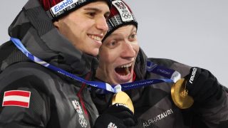 Gold medallists Austria's Stephan Embacher (L) and Austria's Jan Hoerl celebrate on the podium for the men's large hill super team ski jumping of the Milano Cortina 2026 Winter Olympic Games at Predazzo Ski Jumping Stadium in Predazzo (Val di Fiemme), on February 16, 2026.
