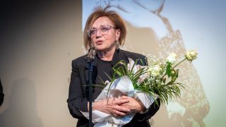 Csákányi Eszter virágcsokorral a kezében beszél a mikrofonba a 2025-ös Psota-díjátadón