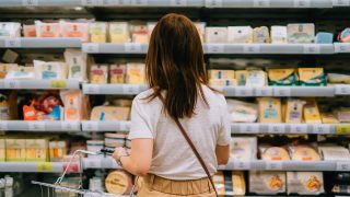 Young woman choosing dairy products from the refrigerator in supermarket. Healthy eating and lifestyle.