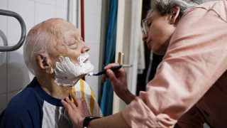 Egy szociális munkás borotválja idős gondozottját