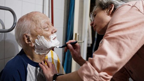 Egy szociális munkás borotválja idős gondozottját
