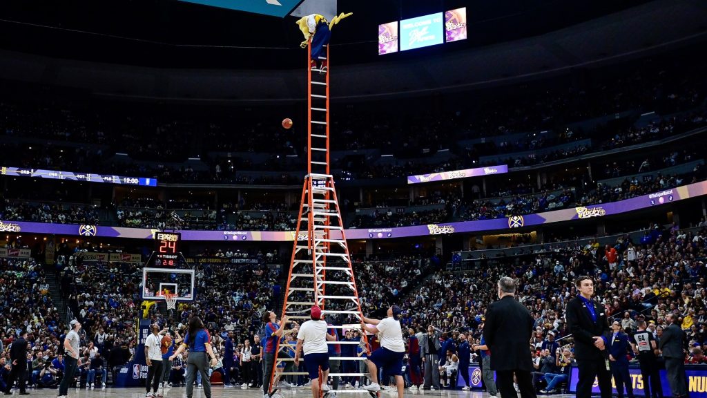Létrán állva, a palánknak háttal dobott félpályás kosarat az NBA-csapat kabalafigurája