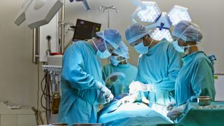Műtősök műtenek egy műtő asztalon, amin egy beteg fekszik