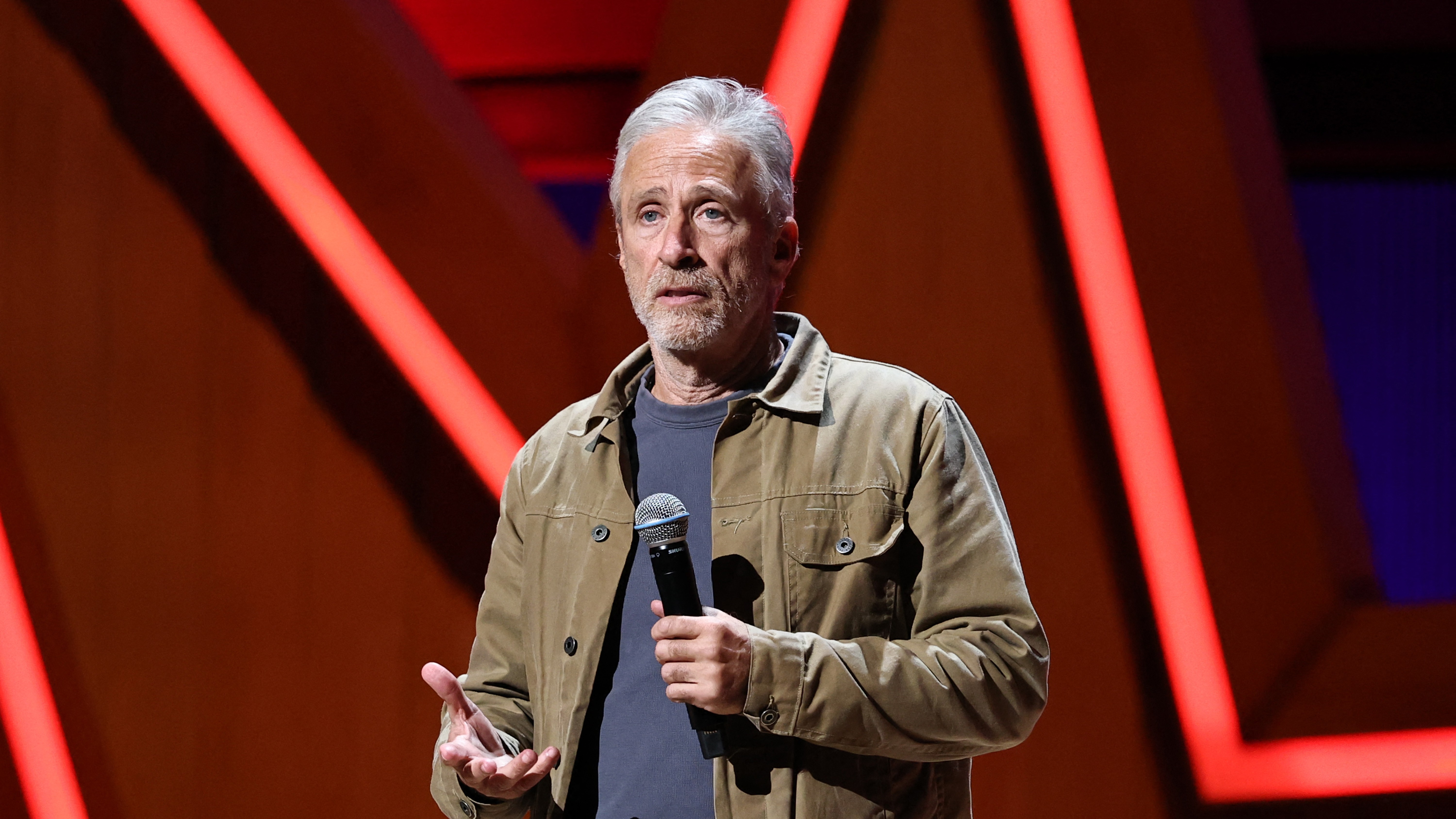 Jon Stewart mikrofonnal a kezében áll egy színpadon.