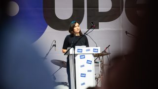 Pottyondy Edina egy pódium mögött beszél egy színpadon.