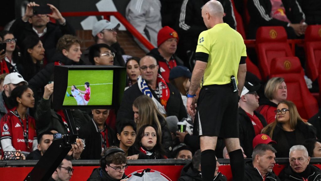 English referee Paul Tierney watches a hair-pulling incident involving Manchester United's Argentinian defender #06 Lisandro Martinez and Leeds United's English striker #09 Dominic Calvert-Lewin on a pitch-side monitor resulting in a red card for Martinez during the English Premier League football match between Manchester United and Leeds United at Old Trafford in Manchester, north west England, on April 13, 2026.
