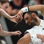 A member of the ground staff helps Serbia's Novak Djokovic to cut a piece of his kinesio tape during a break of his men's singles second round tennis match against Greece's Stefanos Tsitsipas on the third day of the 2026 Wimbledon Championships at The All England Lawn Tennis and Croquet Club in Wimbledon, southwest London, on July 1, 2026.