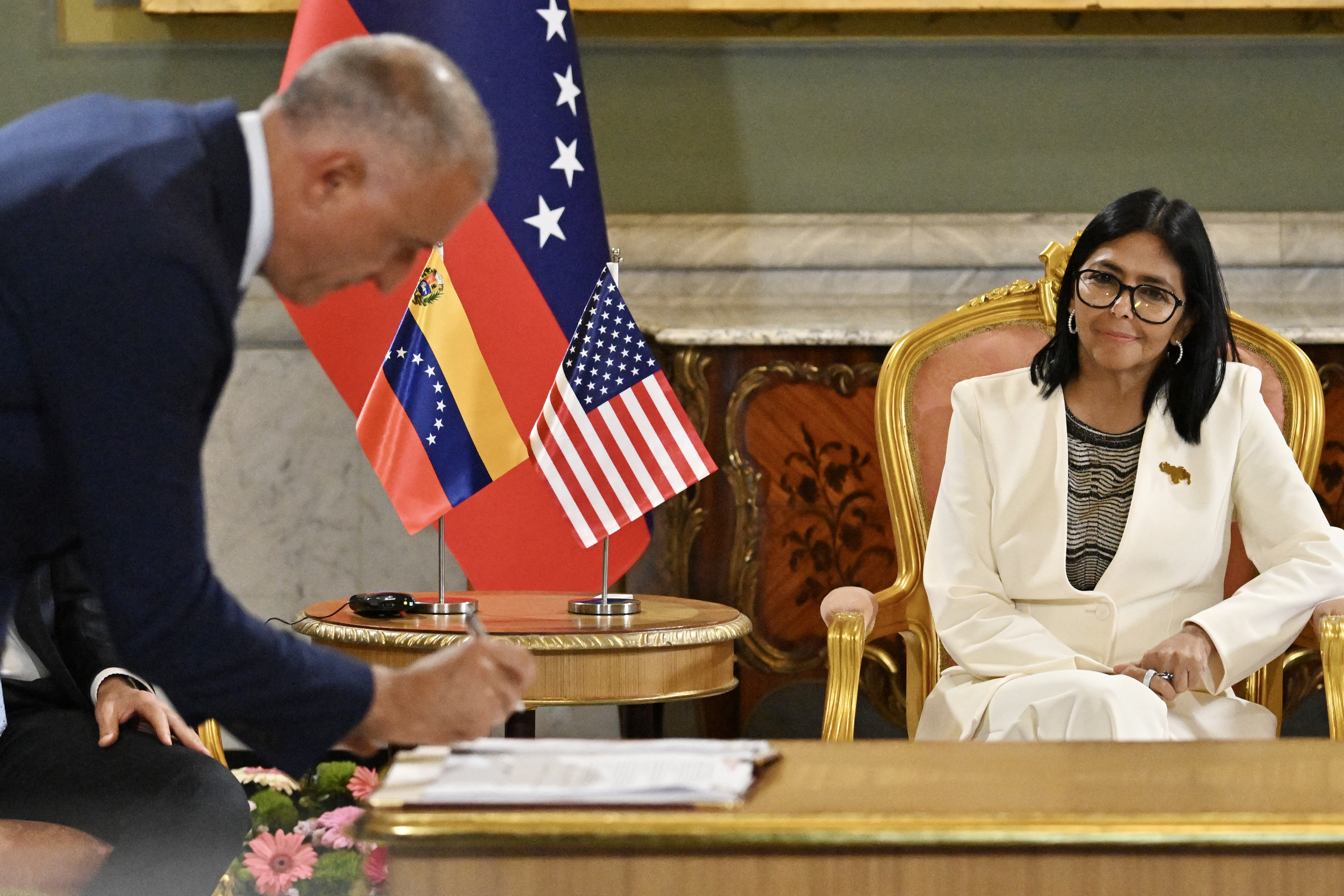 Trumpnak az a legfontosabb a venezuelai olajban, hogy elszívhassa a riválisai elől 1 A man in a dark suit bows toward a woman in a white suit seated at a table, with U.S. and other flags in the background.