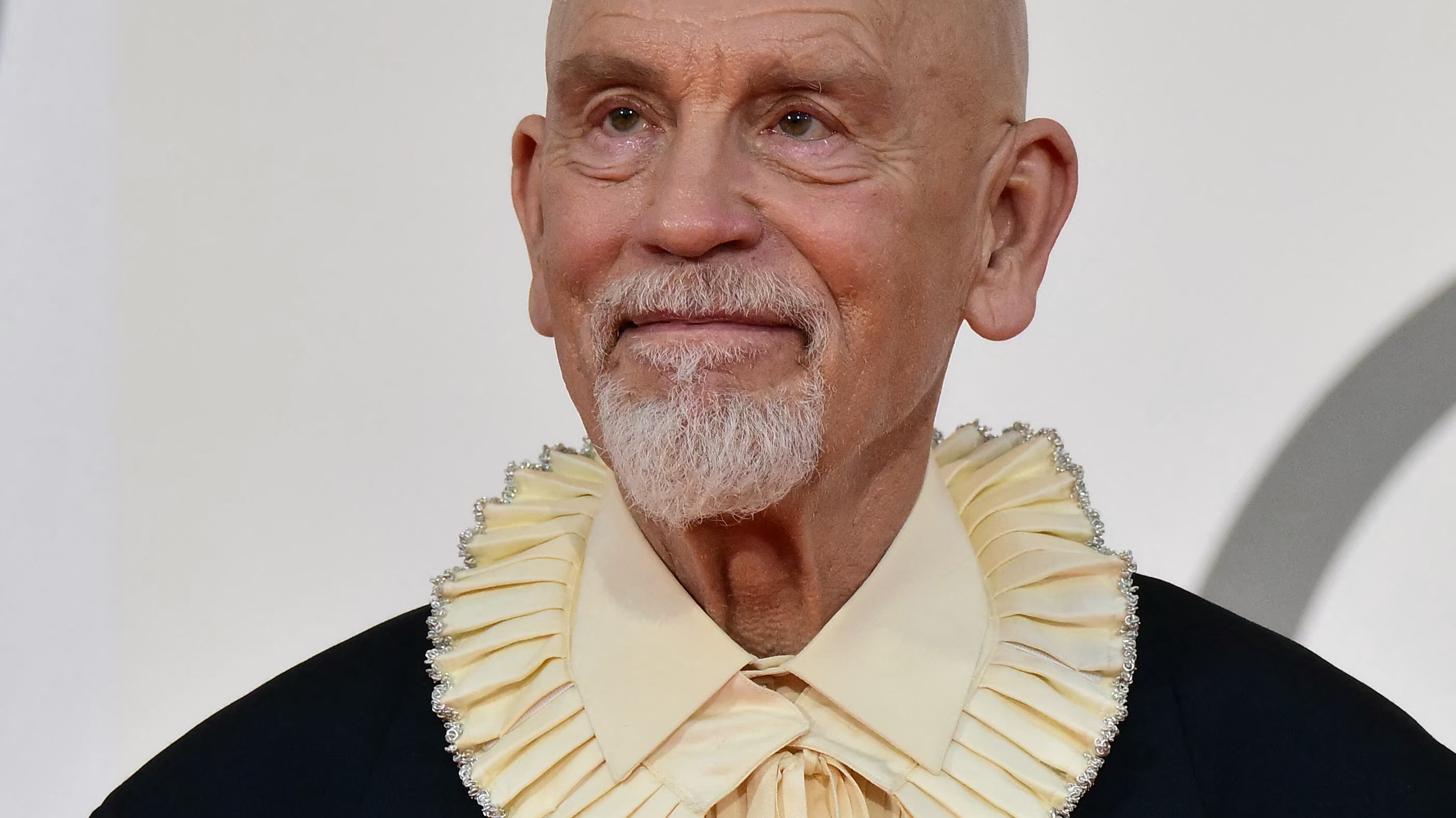 Close-up portrait of an older man wearing a cream pleated ceremonial collar with a black jacket, facing forward
