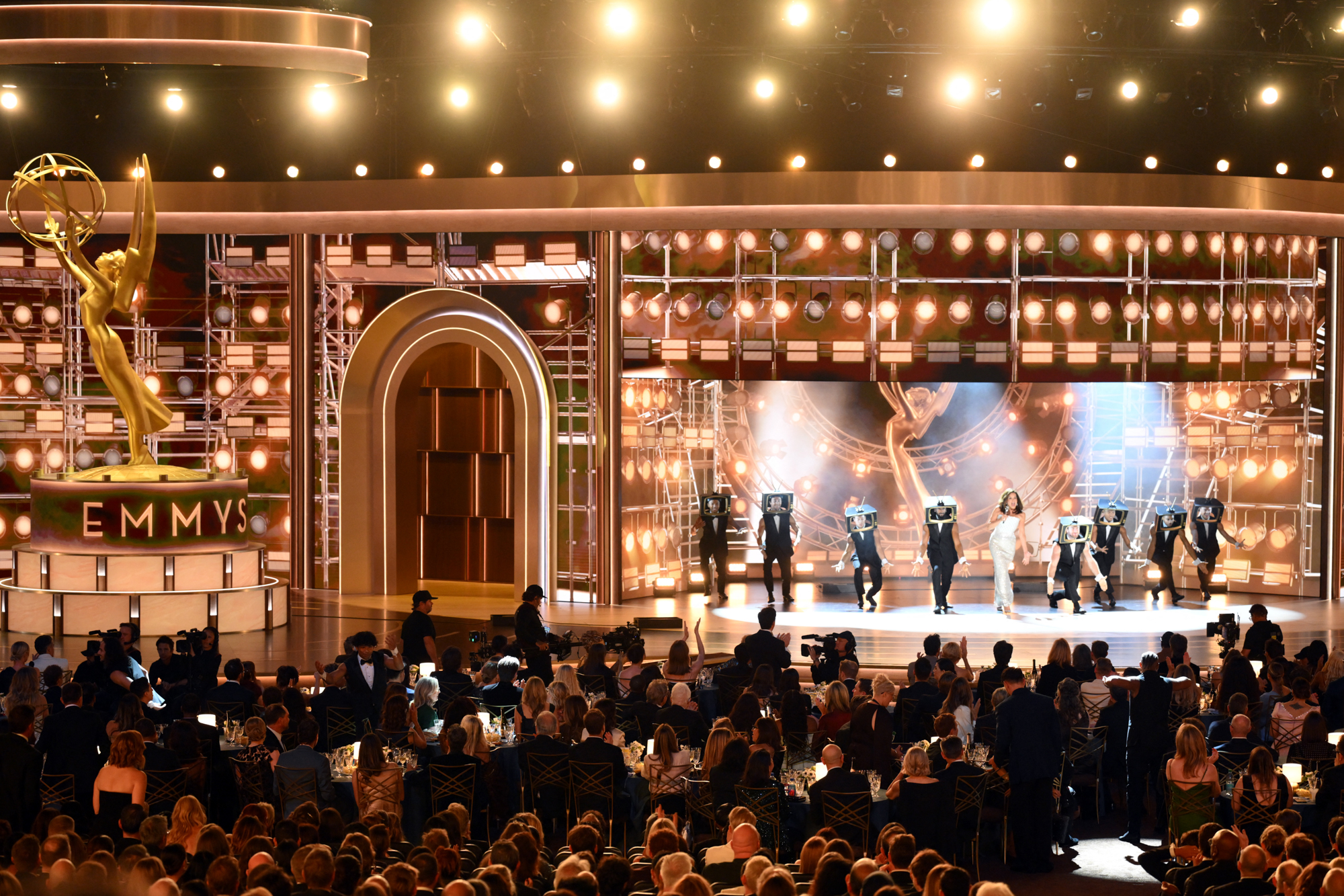 Golden Emmy statue on a circular pedestal on a lit stage at an awards ceremony, with audience in front.