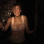Woman with wet hair and a stained white tank top stands in a dark room, arms outstretched and smiling.