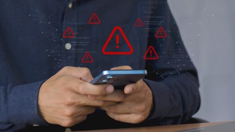 Person using a smartphone with red warning icons and circuit-like graphics representing cybersecurity alerts on screen overlayed