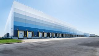 Long industrial warehouse with multiple loading docks along a blue gradient facade.