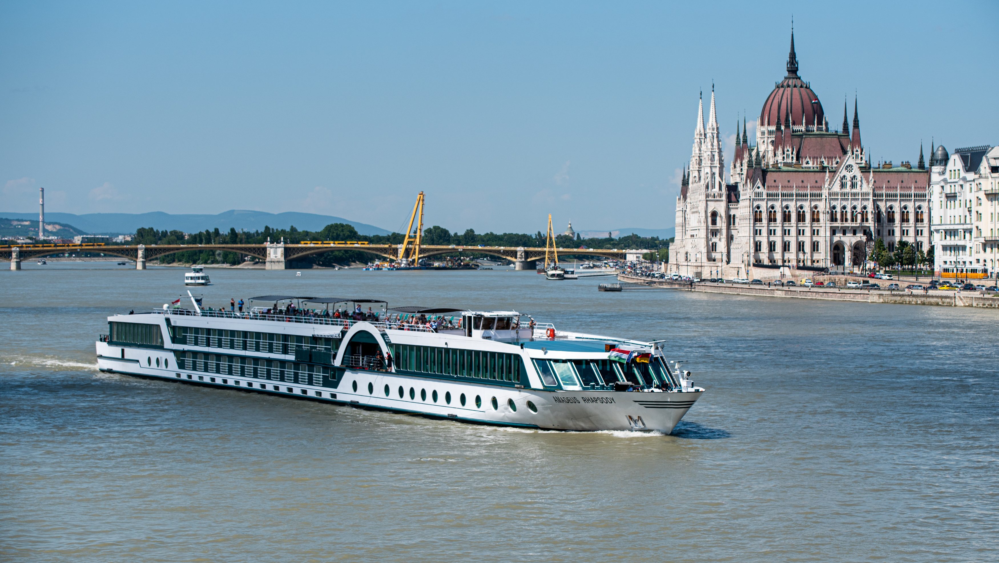 White passenger cruise ship on the Danube near Budapest's Parliament Building with a bridge and riverfront in the background.