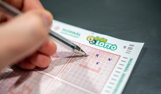 Close-up of a hand scratching a red-bordered lottery ticket; the LOTTO logo is visible near the top edge.