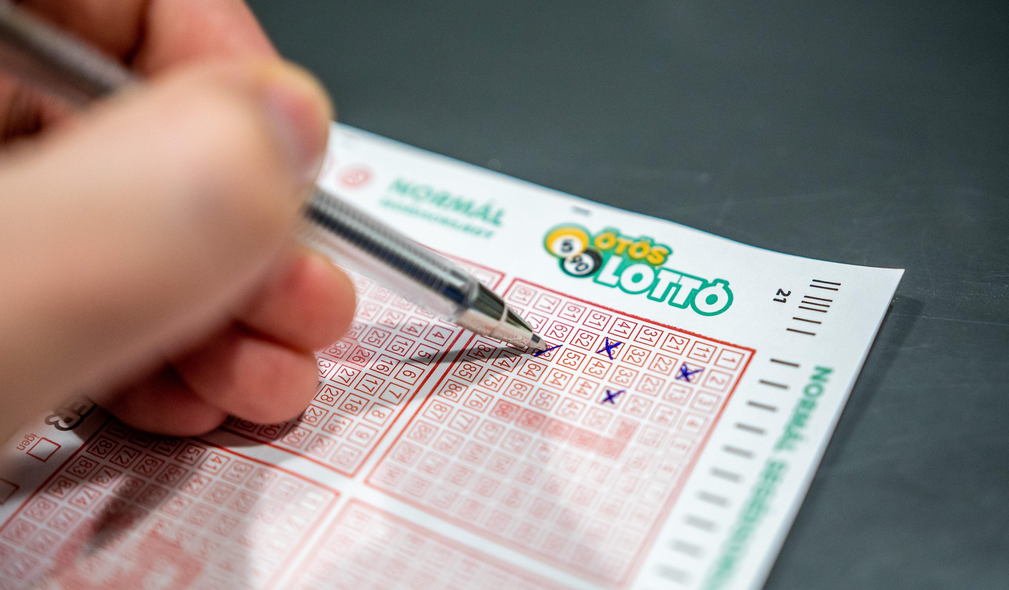 Close-up of a hand scratching a red-bordered lottery ticket; the LOTTO logo is visible near the top edge.