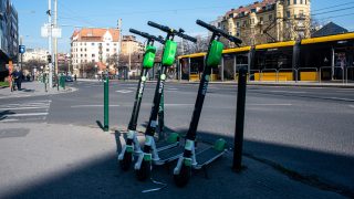 Green Lime e-scooters leaning together on a city street foreground with a yellow tram passing behind them.