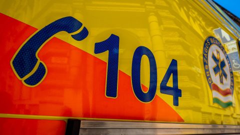 Close-up of a bright yellow ambulance side with large blue number 104 on an orange diagonal stripe and a blue Star of Life badge visible on the right edge.