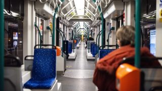 Interior of a subway car viewed down the aisle, blue patterned seats and teal poles with hanging straps.