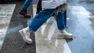People crossing a wet street on a zebra crosswalk, focusing on legs and footwear.