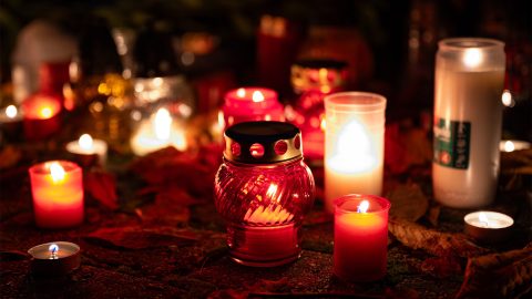 Close-up of lit candles and lanterns on a dark outdoor surface, glowing red and white with autumn leaves scattered around.