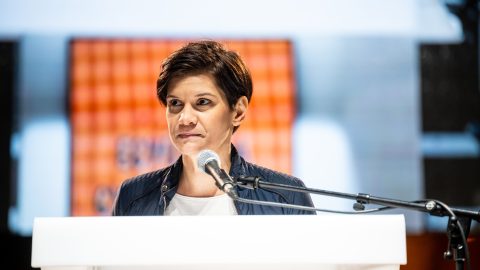 Female speaker at a white podium delivering a talk, microphone in front of her.
