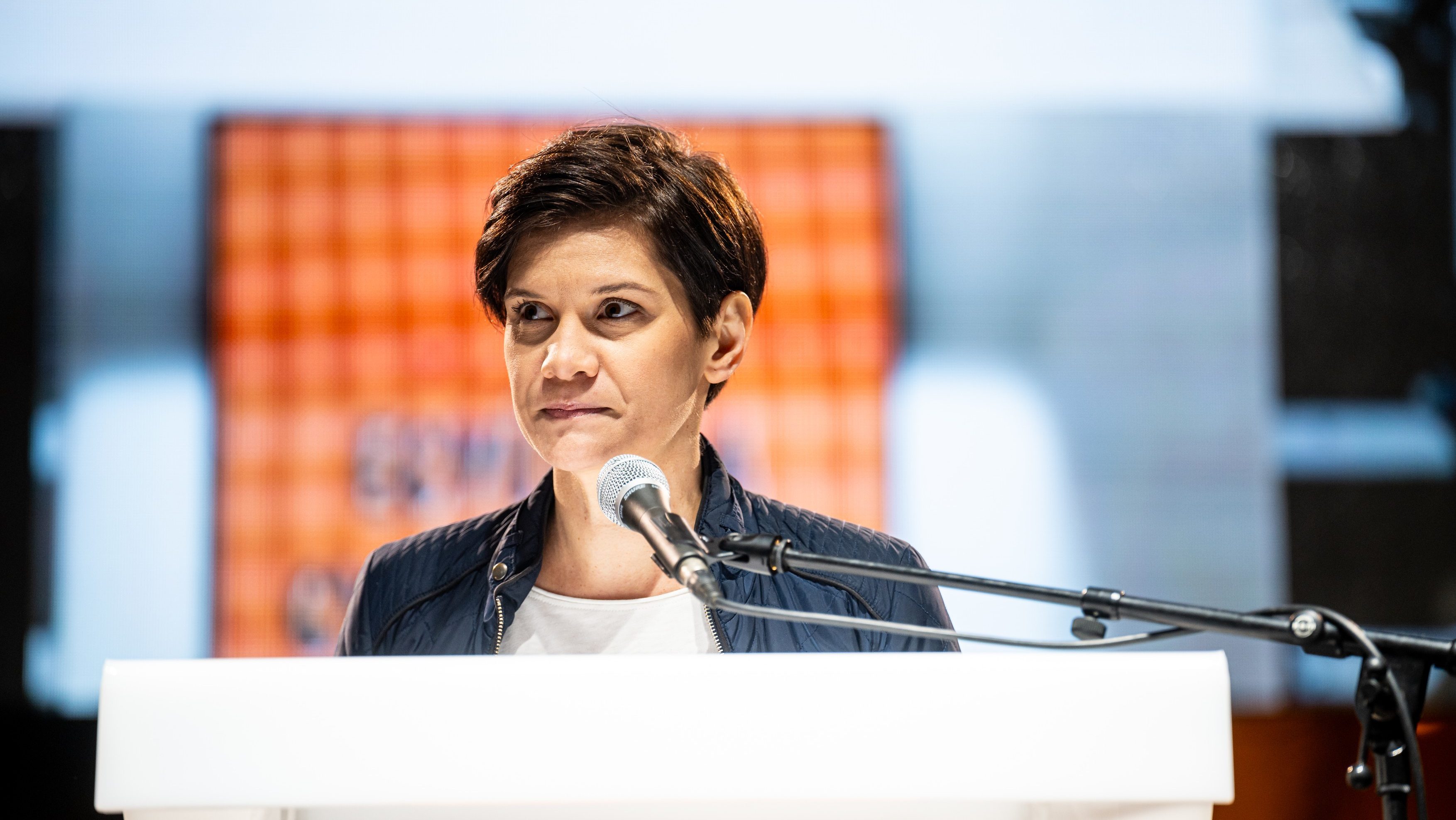 Female speaker at a white podium delivering a talk, microphone in front of her.