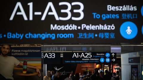 Airport sign listing A1–A33 and directions to gates, toilets and baby-changing room with travelers below.