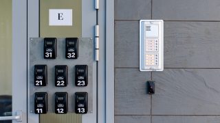 Row of black combination locks labeled 11–13, 21–23, and 31–33 next to a metal door on a gray wall with an intercom panel nearby.