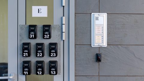 Row of black combination locks labeled 11–13, 21–23, and 31–33 next to a metal door on a gray wall with an intercom panel nearby.