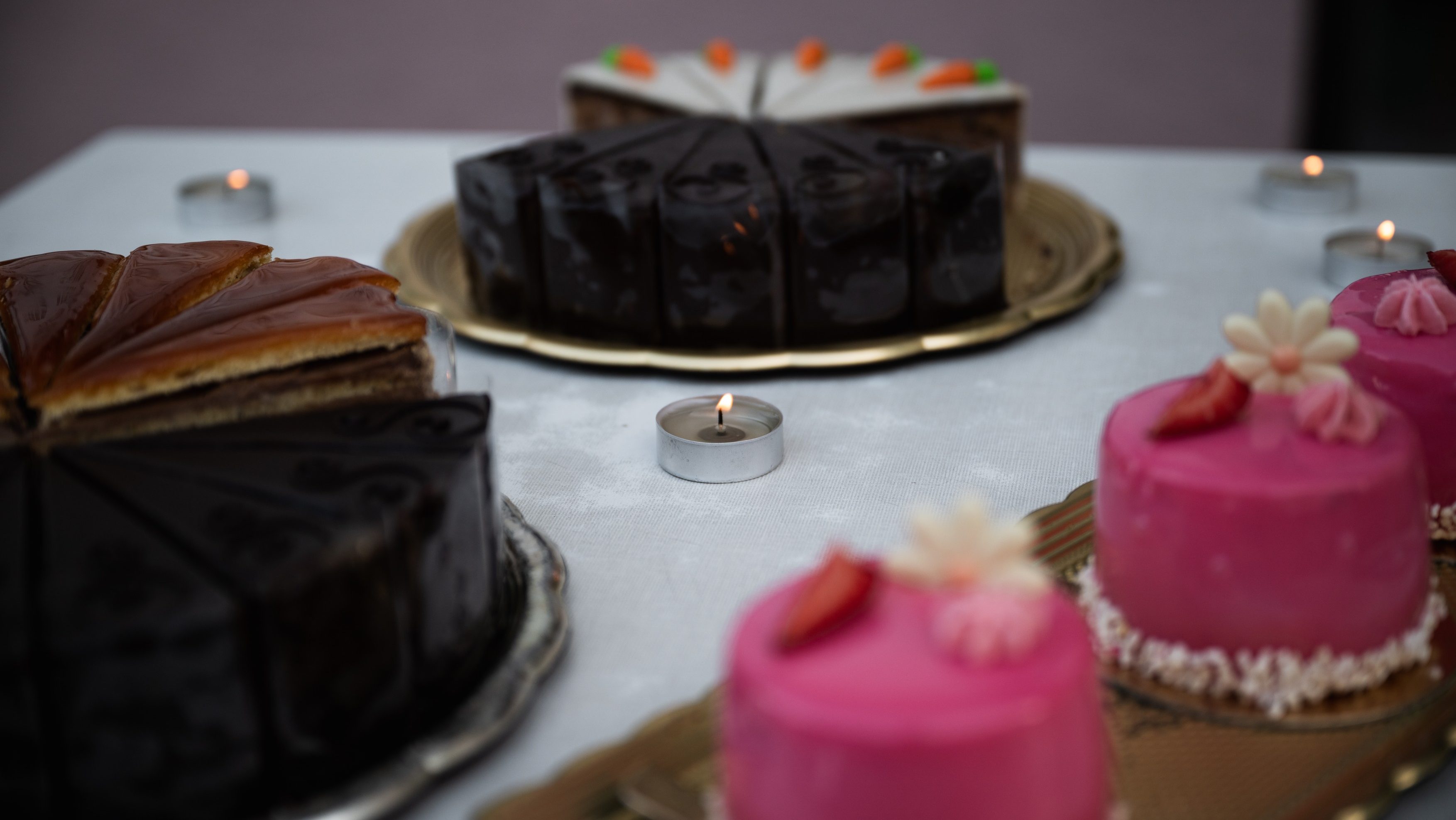Assorted cakes on a table with tealight candles; pink frosted cupcakes in foreground and chocolate cake in background.