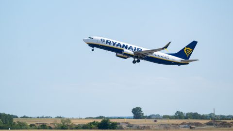 Ryanair airplane lifting off a runway, wheels down, blue sky in the background.