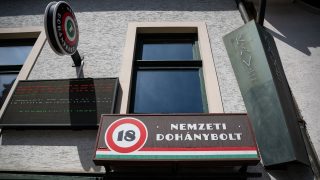 Signboard reads 'Nemzeti Dohánybolt' with a circular 18 logo on a building facade and an electronic display panel to the left.