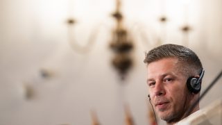 Portrait of a man wearing a headset, looking toward the camera, in a softly blurred indoor setting (call center/office).