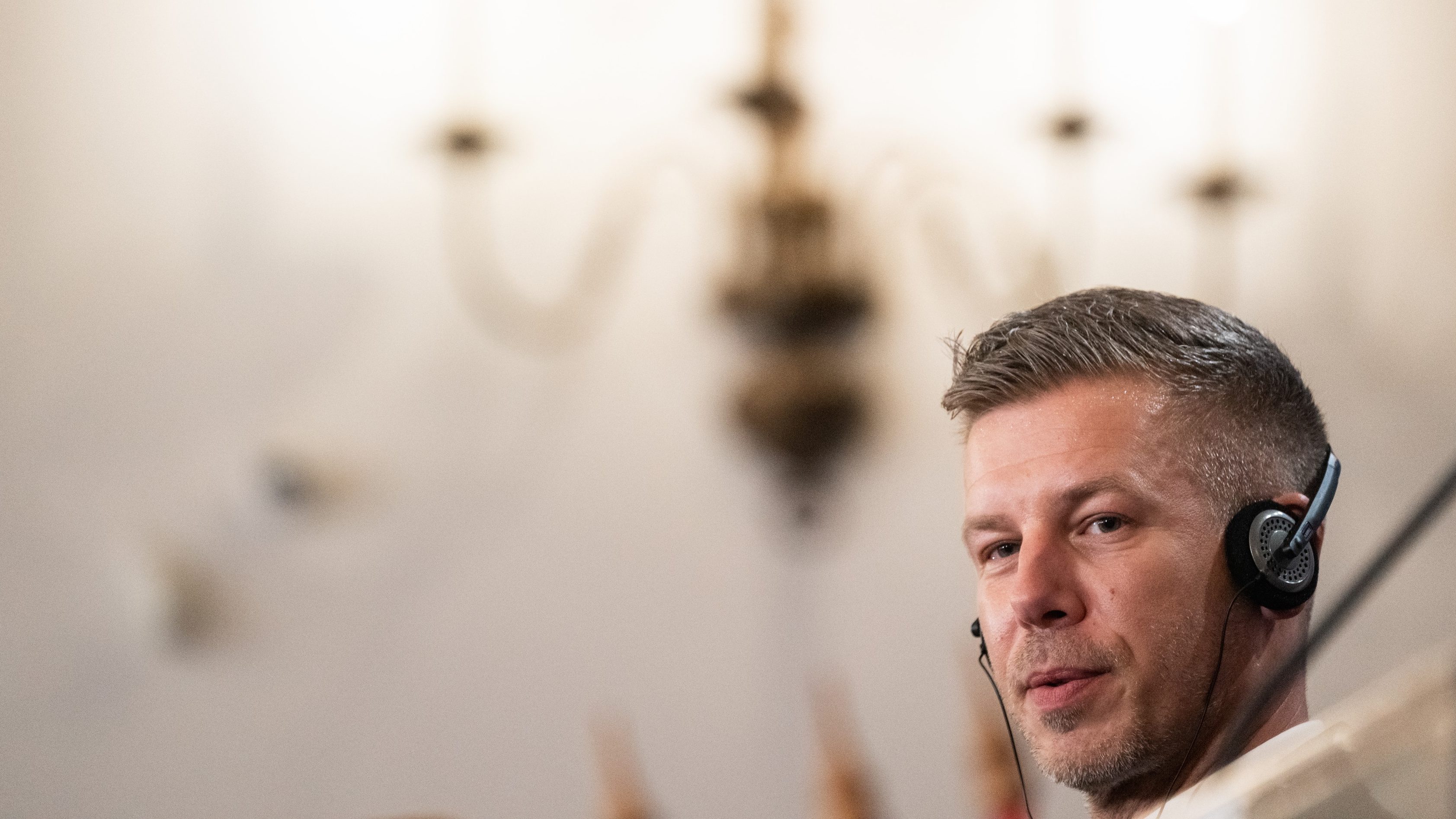 Portrait of a man wearing a headset, looking toward the camera, in a softly blurred indoor setting (call center/office).