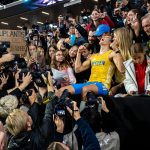 Swedish runner in a yellow Sweden kit celebrating while photographers crowd around him at a press event.