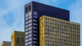 Modern glass office towers with yellow and dark paneling against a clear blue sky.