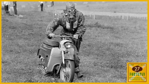 Person in a gas mask rides a vintage scooter across a grassy field; historical photo.