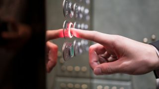 Finger pressing a red-lit floor button on an elevator control panel.