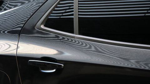 Close-up of a dark car door with chrome trim and a window, showing reflections on the bodywork