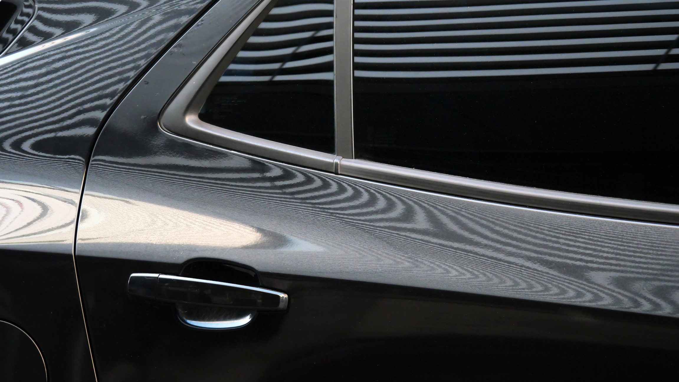Close-up of a dark car door with chrome trim and a window, showing reflections on the bodywork