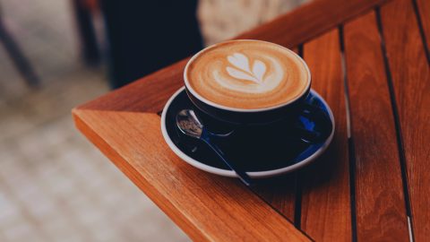 A cup of latte with heart-shaped latte art on a wooden table outdoor setting, viewed from above.