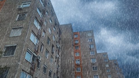 Tall apartment blocks under heavy rain with streaks across a cloudy sky
