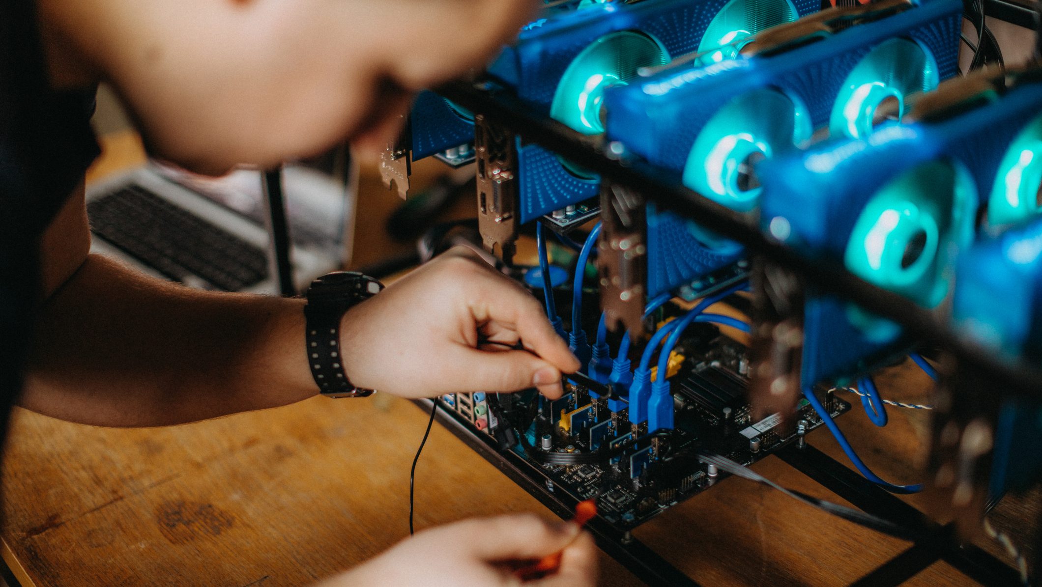 Close-up of hands assembling a computer motherboard inside an open PC case with blue LED cooling fans.